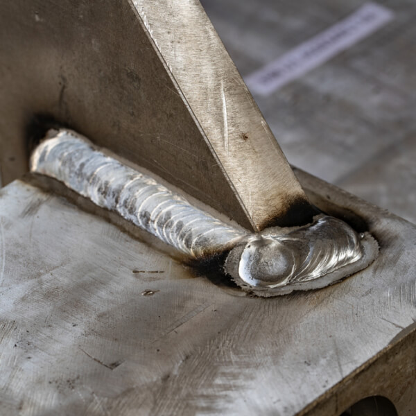 Un gros plan des mains d'un soudeur professionnel manipulant avec précision une torche de soudage sur une pièce métallique, illustrant la maîtrise de la technique.