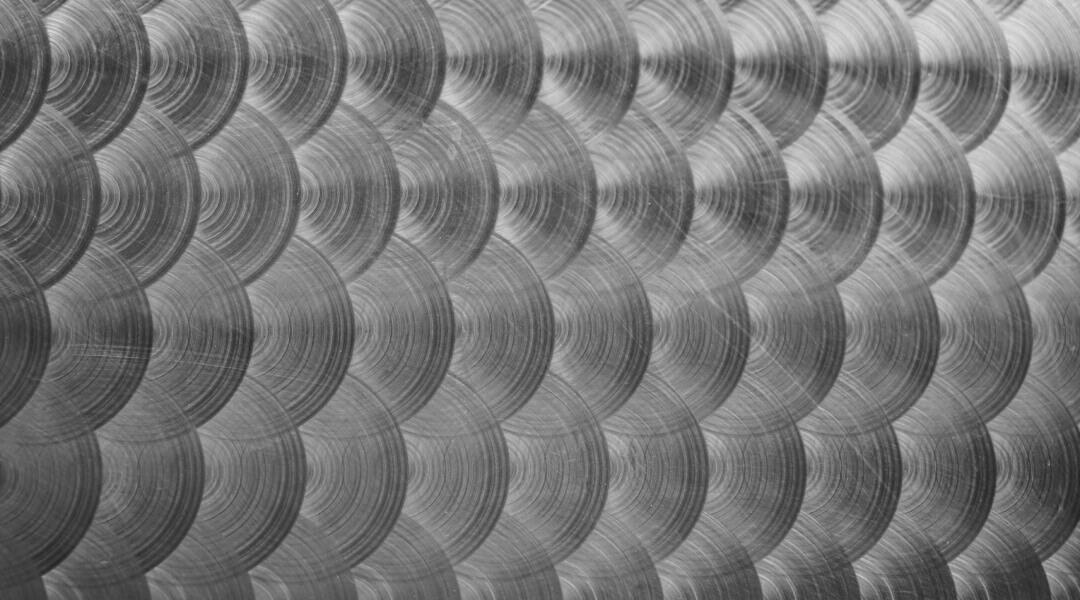 Un gros plan de plusieurs pièces cylindriques identiques en acier brillant, avec des extrémités filetées et des finitions métalliques lisses, soigneusement alignées sur une table d'atelier.