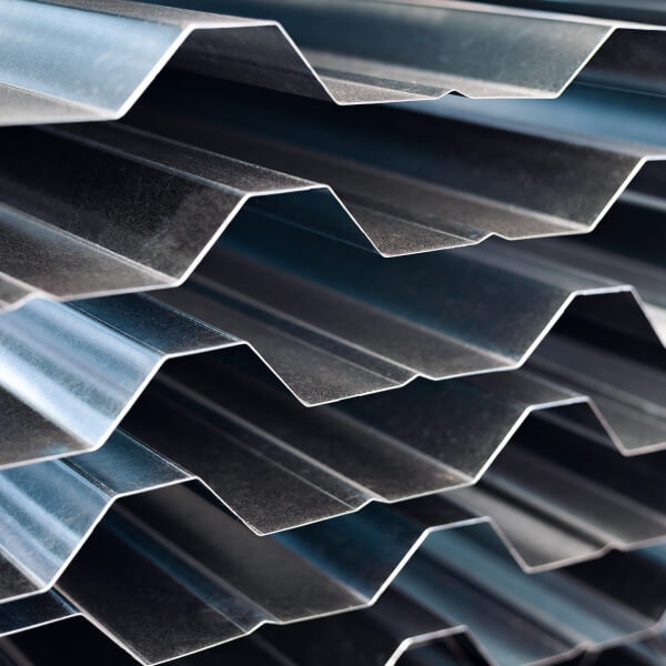 Une vue latérale de plusieurs poutres en I en acier galvanisé à chaud, soigneusement empilées les unes sur les autres à l'extérieur d'une usine de fabrication ou d'un site de construction.