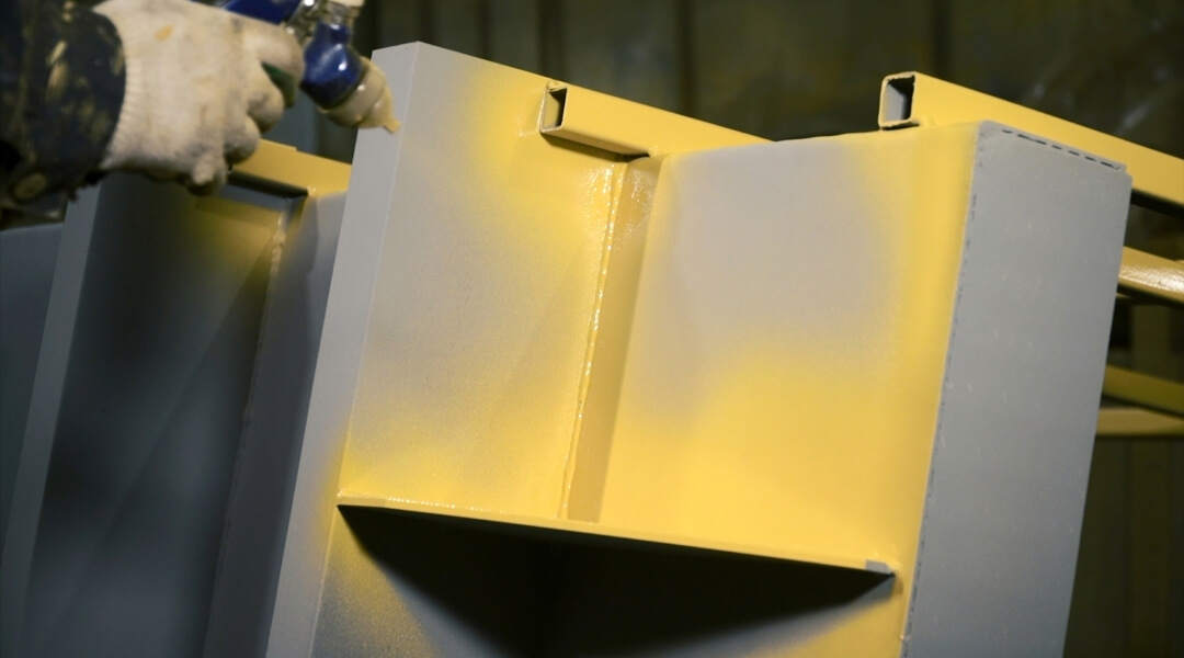 Un bras robotique automatisé équipé d'une buse de pulvérisation appliquant un revêtement protecteur de précision sur une série de cadres métalliques jaunes dans une usine de haute technologie.
