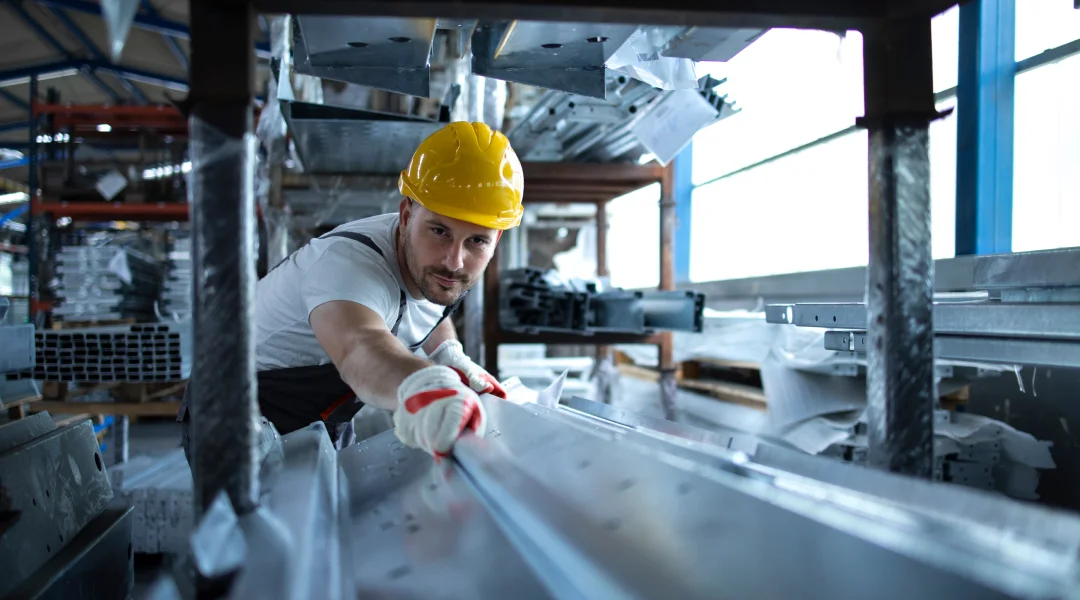 Un homme en casque de sécurité travaille sur un produit métallique dans un atelier de fabrication de structures métalliques.