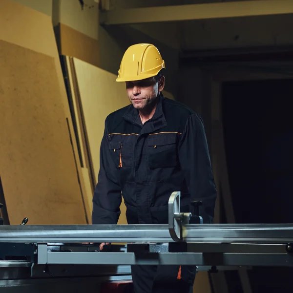 Un homme en casque et en salopette travaille sur une table dans un atelier de fabrication de structures métalliques.